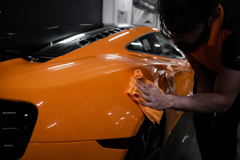 Technicien polissant la carrosserie orange d'une McLaren avec une microfibre