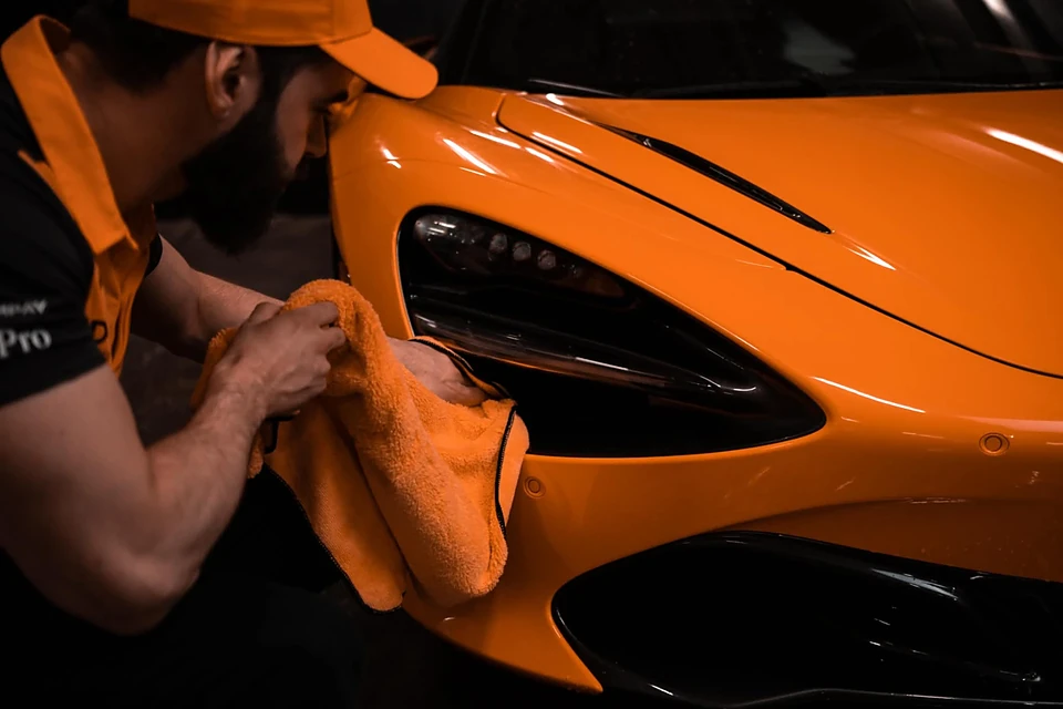Technicien essuyant une McLaren orange à la microfibre orange lors d'un traitement céramique